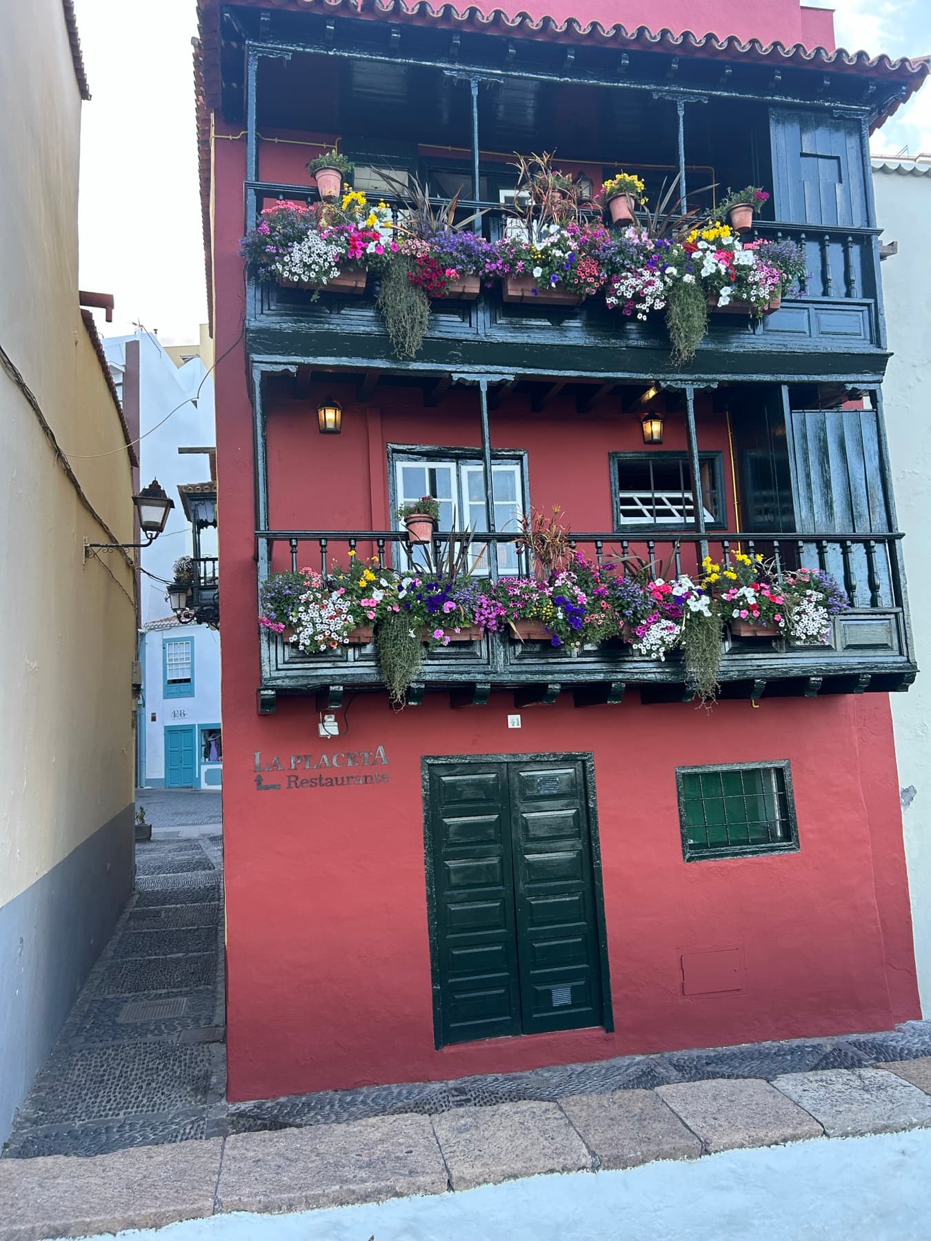 Fachada roja con balcón lleno de flores